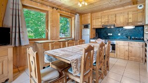 A wooden cabin with a dining table, chairs, a kitchen with a microwave, and a refrigerator.