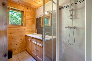 A wooden cabin bathroom with a shower, a sink, and a window.