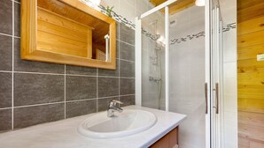 A bathroom with a wooden vanity, a sink, a mirror, and a shower enclosure.