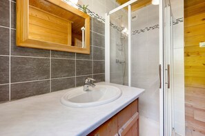 Un baño con tocador de madera, lavamanos, espejo y cabina de ducha.