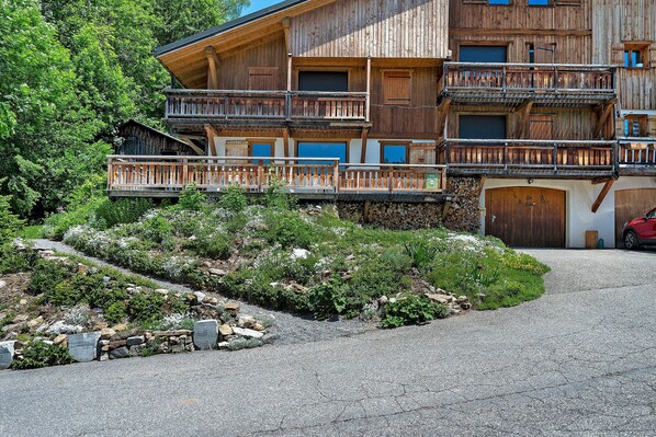 A multi-story wooden building with balconies, a gravel driveway, and a stone wall.