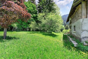 A rustic building with a stone pathway leading to it, surrounded by lush greenery and trees.