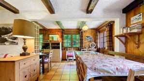 Une pièce rustique avec une table en bois, des chaises, un banc, une lampe, une bibliothèque et une fenêtre avec des rideaux.