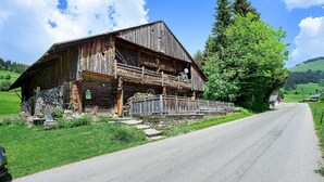Une grange rustique en bois, dotée d’un balcon, entourée d’une végétation luxuriante et surplombant un ciel dégagé.