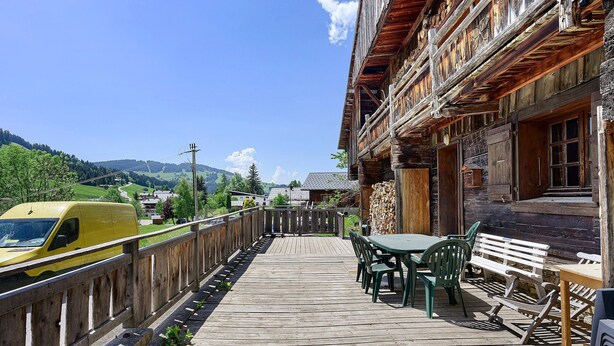 Une terrasse en bois avec des sièges extérieurs, un camionnette jaune et une vue sur la montagne.