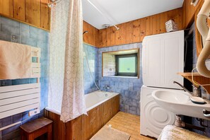 Un baño con bañera, lavamanos, ventana y paredes de madera.