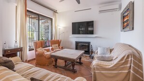 A living room with a sofa, armchair, coffee table, fireplace, TV, and a ceiling fan.