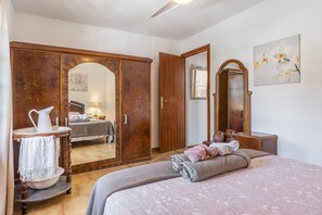 Een slaapkamer met een bed, een houten garderobe, een spiegel en een badkamer door een open deur zichtbaar.