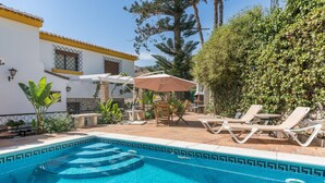 A swimming pool with a tiled edge, lounge chairs, and a patio area with a table and umbrella.