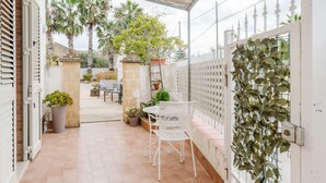 A covered patio area with a table and chairs, potted plants, and a view of the street.