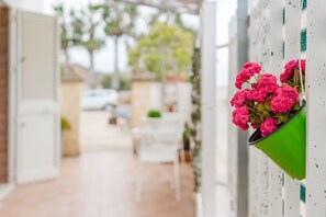 A hallway with a green planter with pink flowers, white walls, and a door leading to a room. - Holiday Home 'Petros' with Shared Terrace, Wi-Fi and Air Conditioning (Marsala)