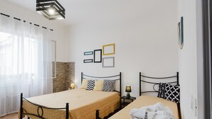 A double bed with a beige bedspread, a bedside table with a lamp, and a wall-mounted picture frame.