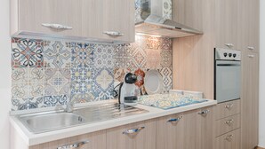 A kitchen with patterned tiles, a stainless steel sink, a coffee machine, and a built-in oven.