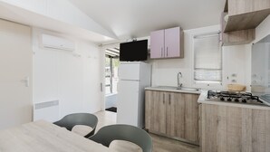 Une cuisine compacte équipée d’un téléviseur à écran plat, de meubles en bois, d’une cuisinière à gaz et d’un coin repas avec des chaises.