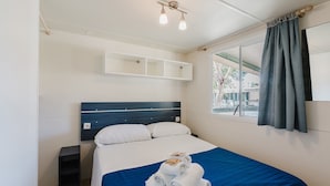 A hotel room with a bed, a nightstand, a window with curtains, and a wall-mounted shelf. - Mobile Home 'Casa Mobile Deluxe' with Shared Pool, Wi-Fi and Air Conditioning (Mazzara del Vallo)