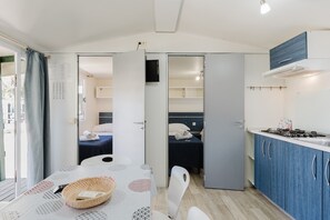 Pieni huone, jossa on sänky, pieni pöytä ja kori, sekä pieni keittiö ja kylpyhuone.