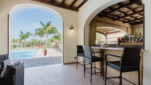 An outdoor bar area with wicker chairs, a pool view, and a bar stocked with bottles. - Mobile Home 'Casa Mobile Deluxe' with Shared Pool, Wi-Fi and Air Conditioning (Mazzara del Vallo)