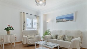 Una sala de estar con sofá, sillones, una mesita de centro, una lámpara y un cuadro de una playa.