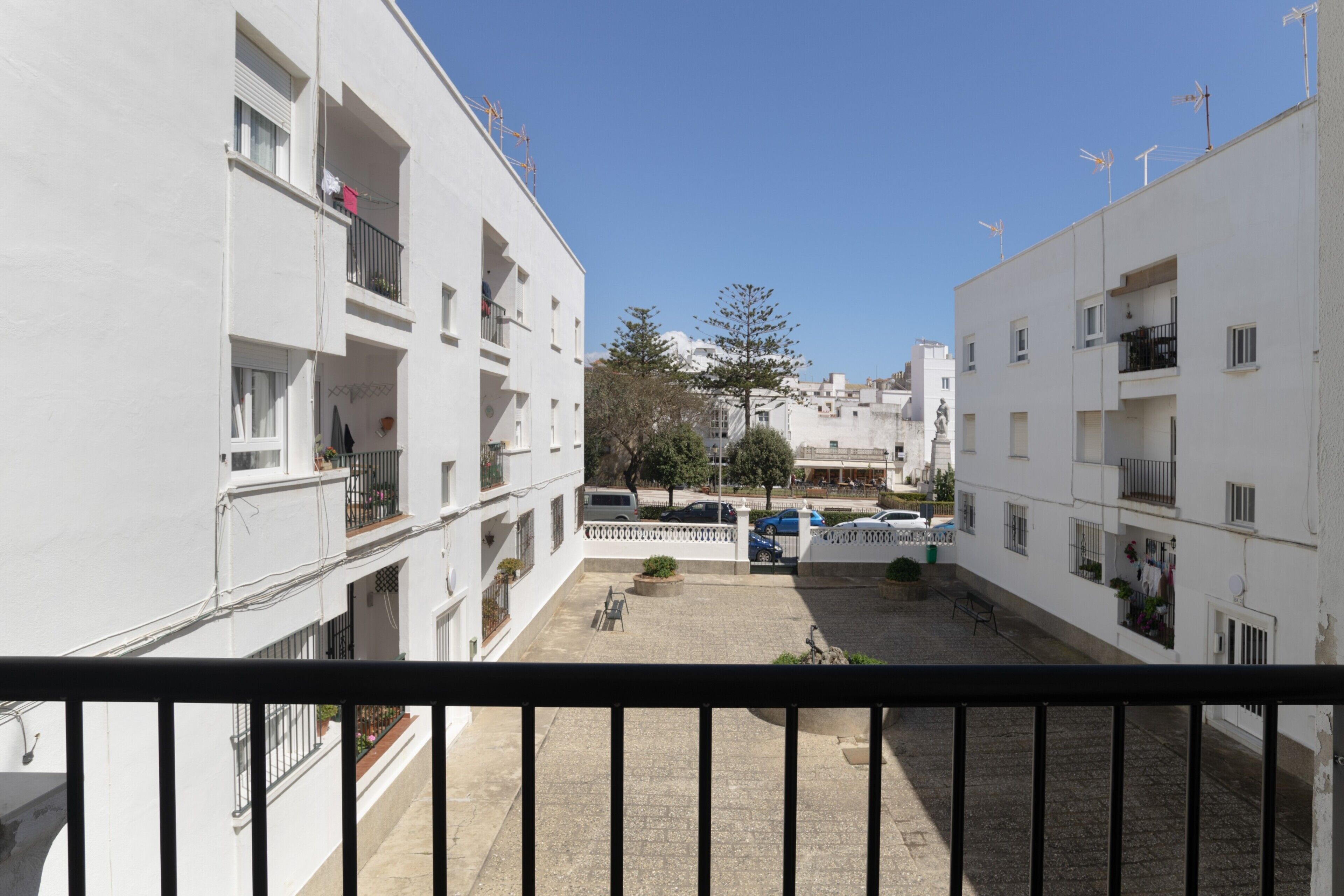 Une cour bordée de bâtiments blancs, de balcons et surplombée d’un ciel dégagé.