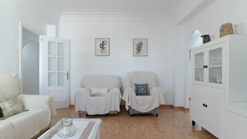 Un salon comprenant deux fauteuils, un canapé, un meuble et deux œuvres d’art accrochées au mur.