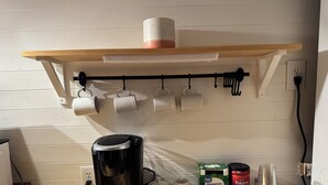 A kitchen with a coffee maker, a shelf with mugs, and coffee cups on the wall. - Charming 1-bedroom mini cottage in enjoyable Punta Gorda with WiFi, AC (Punta Gorda)
