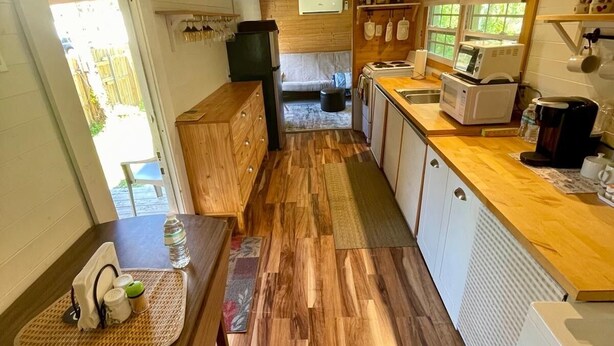 A compact kitchen with wooden flooring, a dining area with a mat, a refrigerator, a microwave, and a coffee maker. - Charming 1-bedroom mini cottage in enjoyable Punta Gorda with WiFi, AC (Punta Gorda)