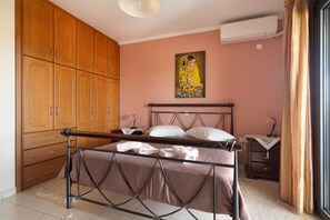 Een slaapkamer met een bed, een houten garderobe, een schilderij aan de muur en een raam met gordijnen.
