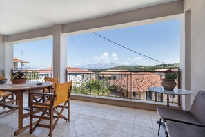 Een balkon met uitzicht op bergen, een zithoek met stoelen en een tafel, en een klein rond tafeltje met een plant.