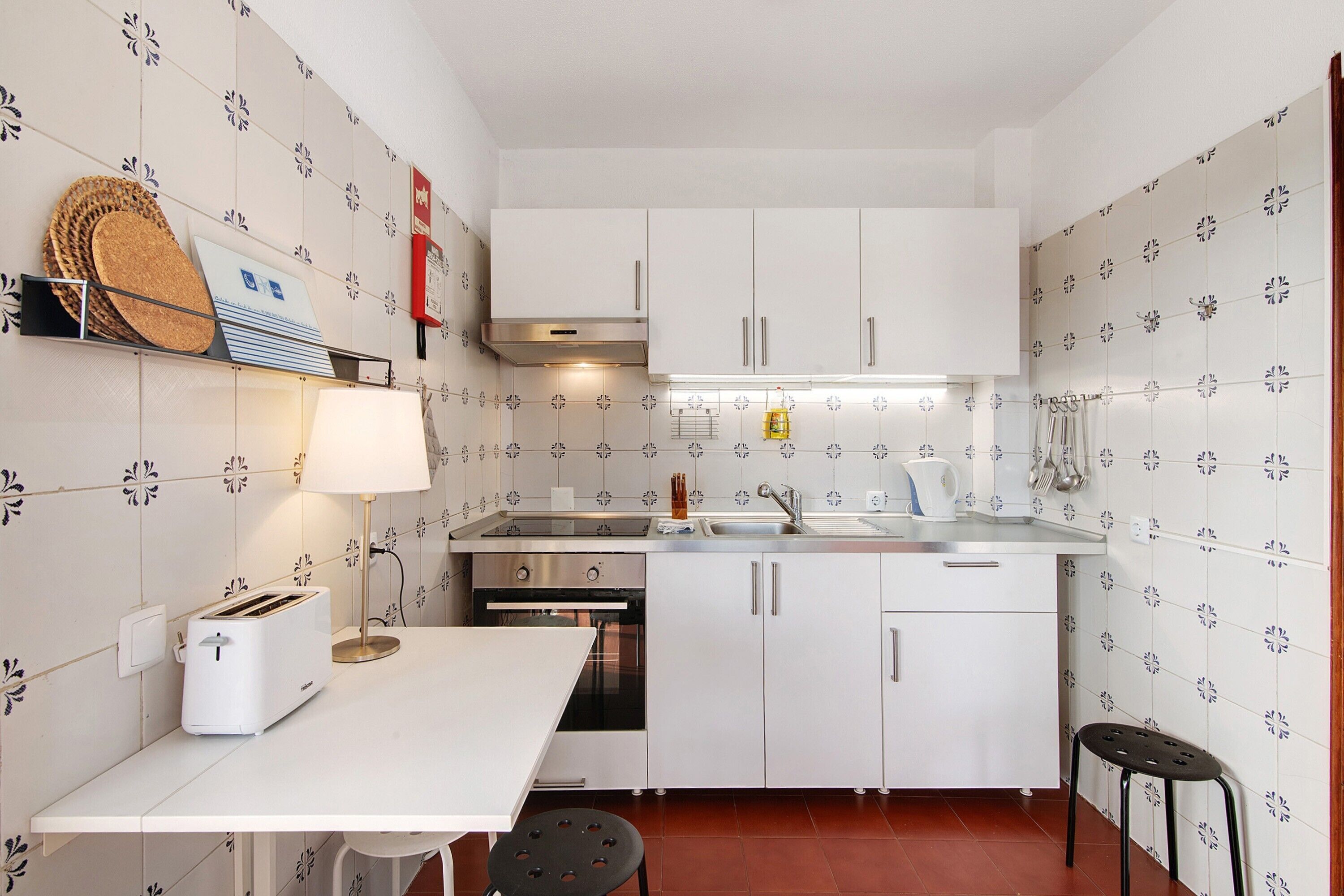Een kleine keuken met witte kastjes, een broodrooster, een spoelbak en een fornuis.