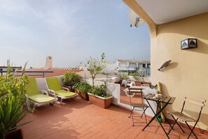 A rooftop terrace with seating, potted plants, and a view of the cityscape.