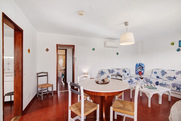 A dining area with a round wooden table, white chairs, and a white sofa with blue patterns.