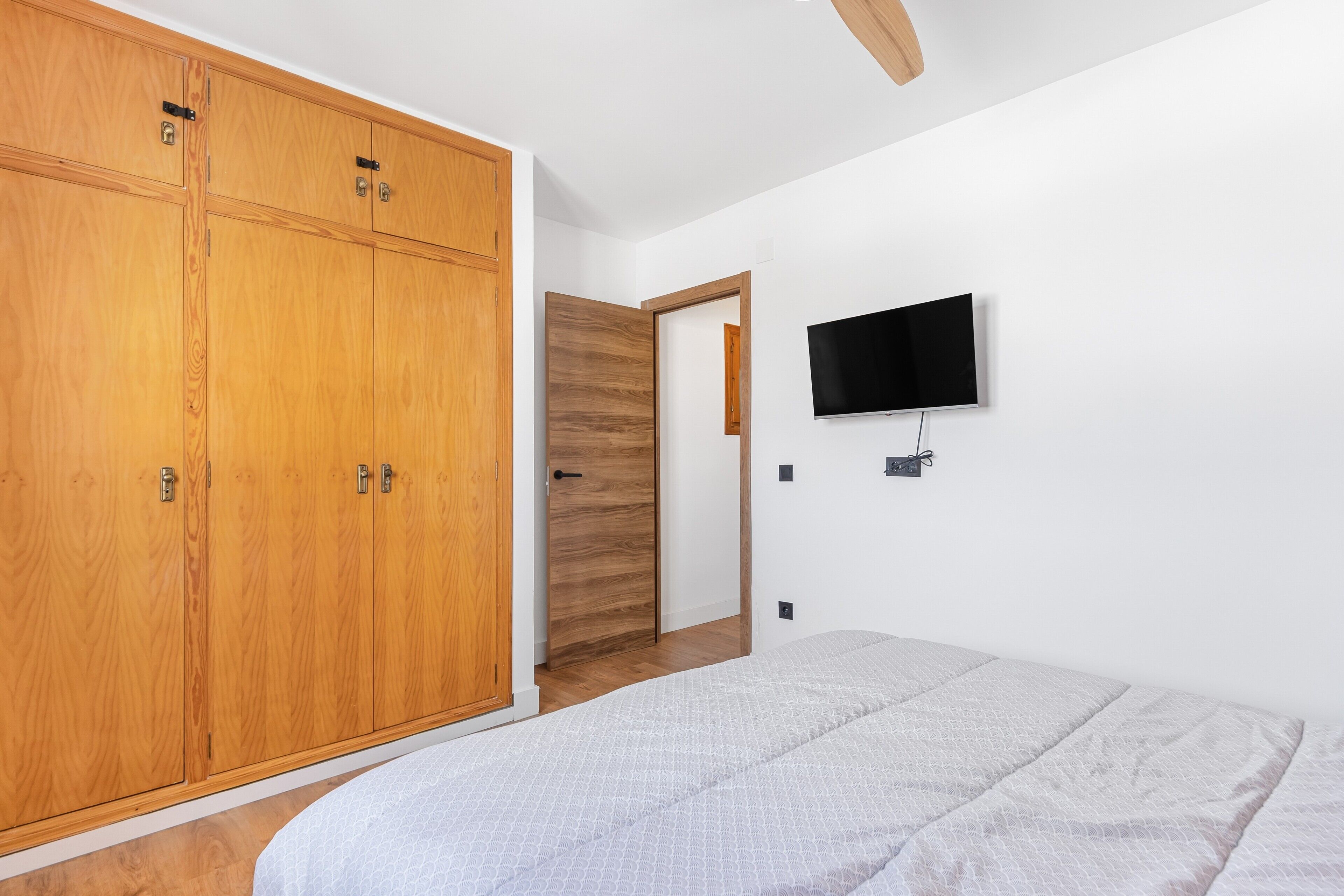Une chambre à coucher comprenant un lit, une armoire, un téléviseur fixé au mur et une porte en bois.
