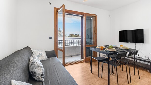 Ein modernes Wohnzimmer mit einer Couch, einem Esstisch, Stühlen, einem Fernseher und einer Glastür zum Balkon.