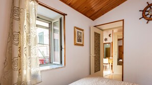 Een slaapkamer met een bed, een raam met gordijnen, een deur naar een badkamer en een aan de muur bevestigd scheepswiel.