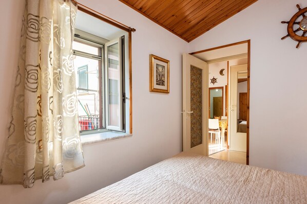 A bedroom with a bed, a window with curtains, a door leading to a bathroom, and a wall-mounted ship's wheel.