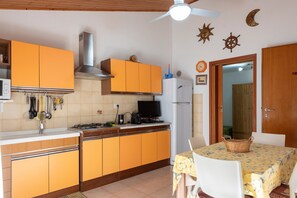 A kitchen with orange cabinets, a white refrigerator, and a dining table with a basket.