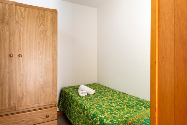 Una habitación pequeña con un armario de madera, una cama individual con colcha verde estampada y una toalla blanca sobre la cama.