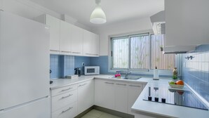 Une cuisine moderne avec des meubles blancs, un four à micro-ondes, un évier et une fenêtre donnant sur une bambouseraie.