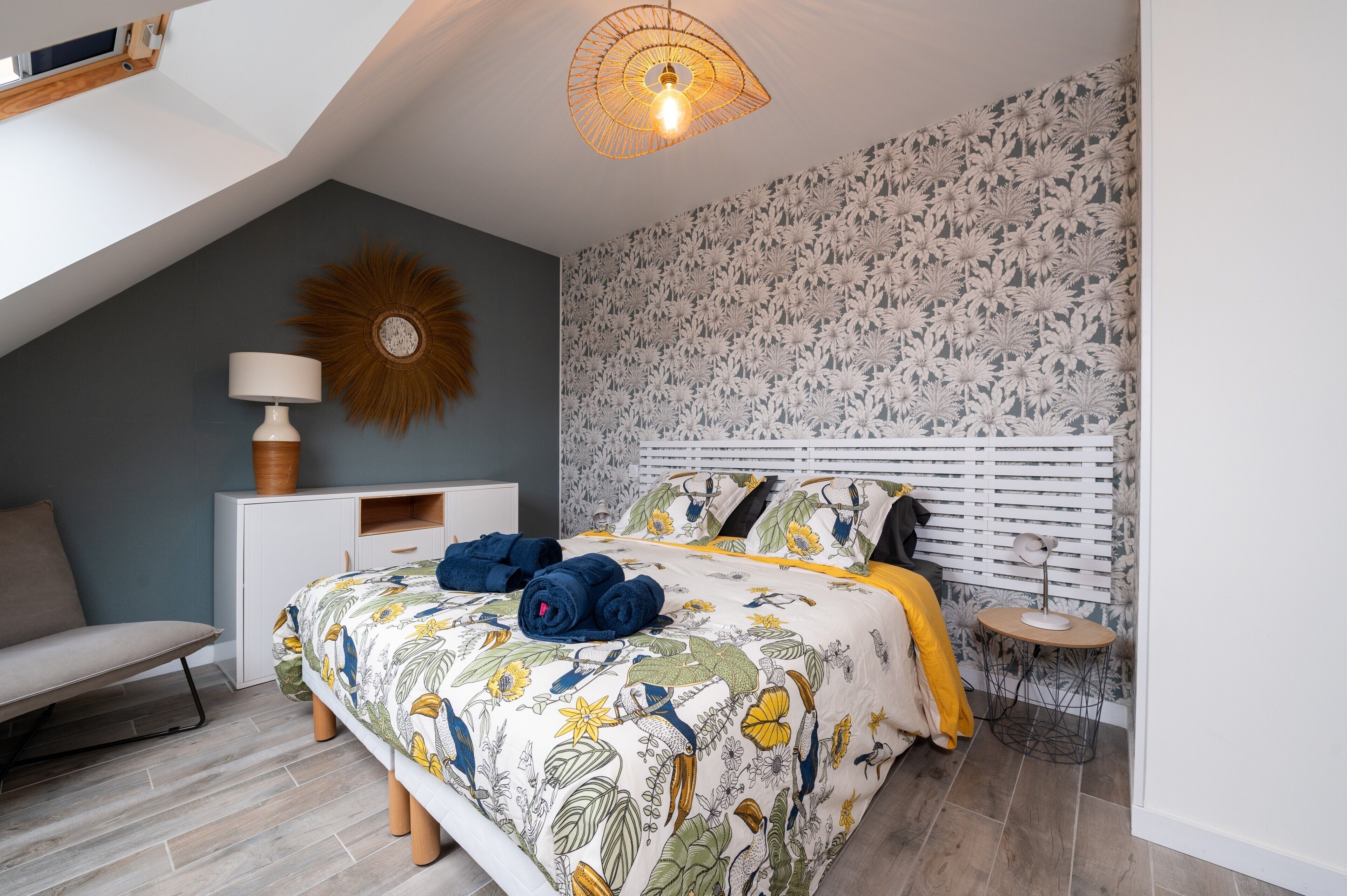 A bedroom with a sloped ceiling, a bed with floral bedding, a bedside table with a lamp, and a patterned wall.