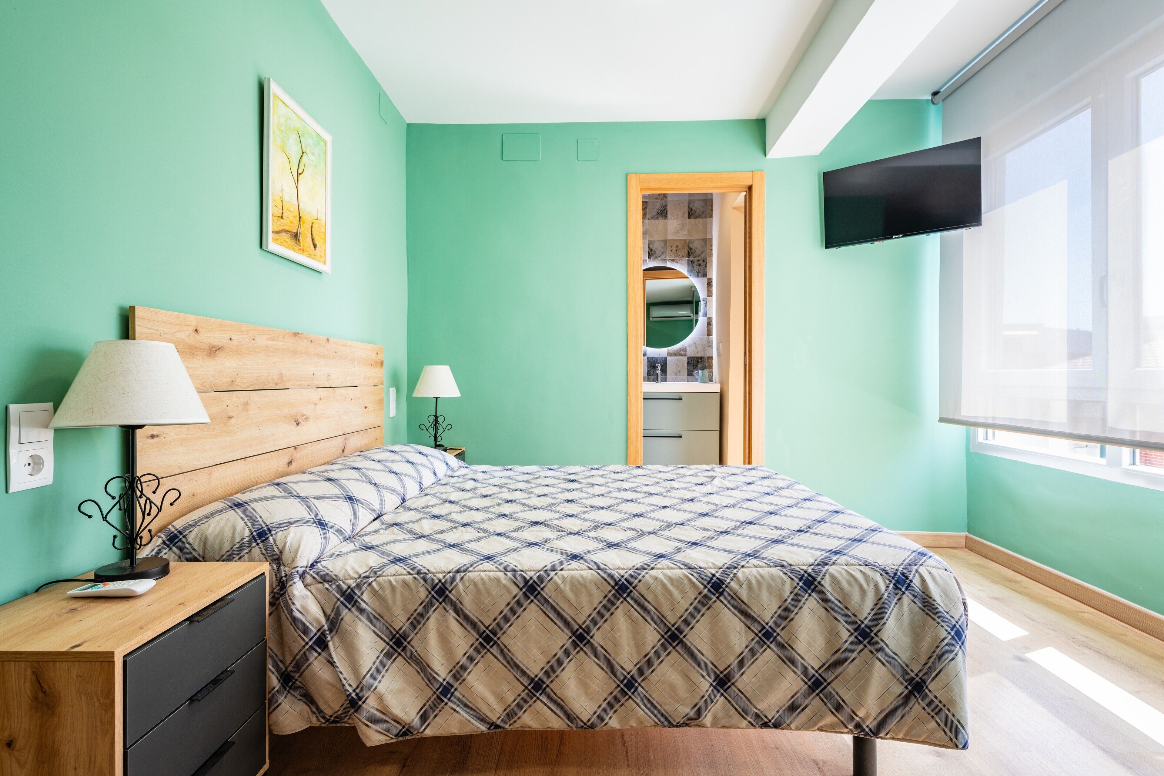 A bedroom with a bed, nightstand, lamp, TV, and a bathroom door.