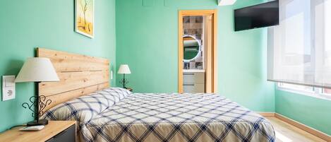A bedroom with a bed, nightstand, lamp, TV, and a bathroom door.