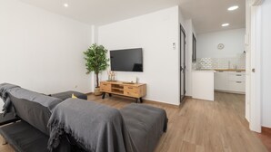 Een moderne woonkamer met een bank, een televisie, een houten kast en een potplant.