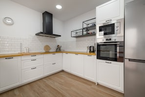 Une cuisine moderne avec des armoires blanches, un plan de travail en bois, une hotte noire, un four encastré et un micro-ondes.
