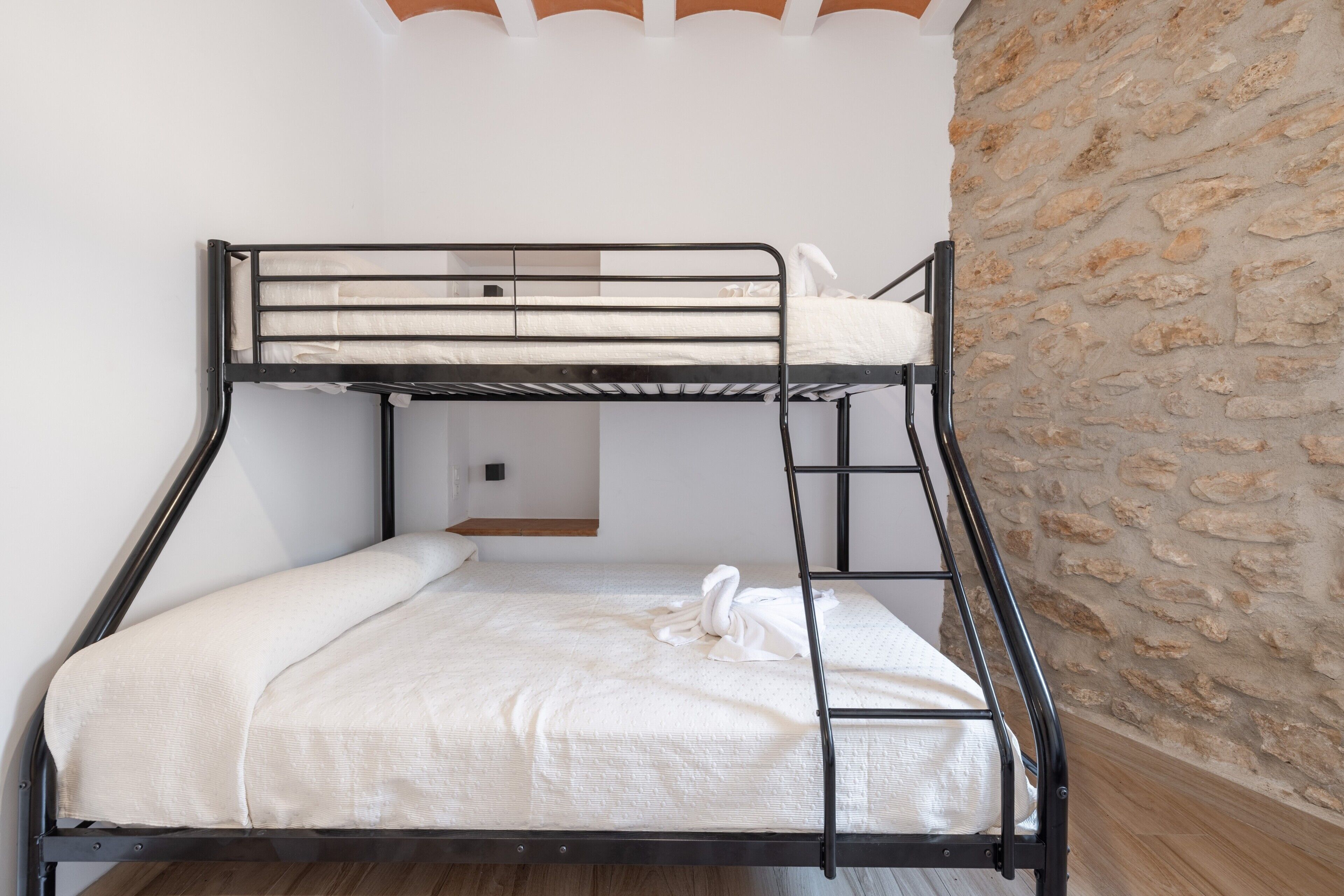 A bunk bed with a white mattress and a towel, a stone wall, and a wooden floor.