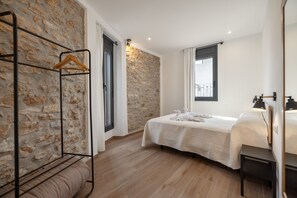 Ein Schlafzimmer mit Steinwand, einem Bett mit weißer Bettdecke, einem Wäscheständer aus Holz und einem Fenster mit Vorhängen.