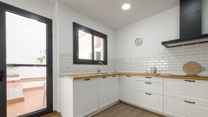 Een moderne keuken met witte kastjes, een houten aanrecht, een zwarte afzuigkap en een raam met uitzicht.
