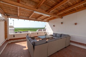 Une terrasse couverte avec un canapé en osier, une table et une vue sur un terrain de sport.