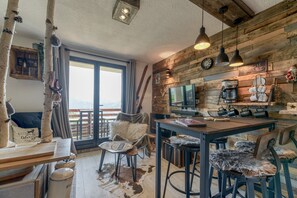 A rustic kitchen with a wooden wall, a coffee machine, and a large window. - Studio 'Exceptional View' with Mountain Views, Balcony, and Wi-Fi (Alpe d'Huez)
