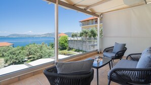 A balcony with wicker furniture, a table, and a view of the sea and mountains.