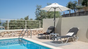 A pool area with lounge chairs, an umbrella, and a stone wall.